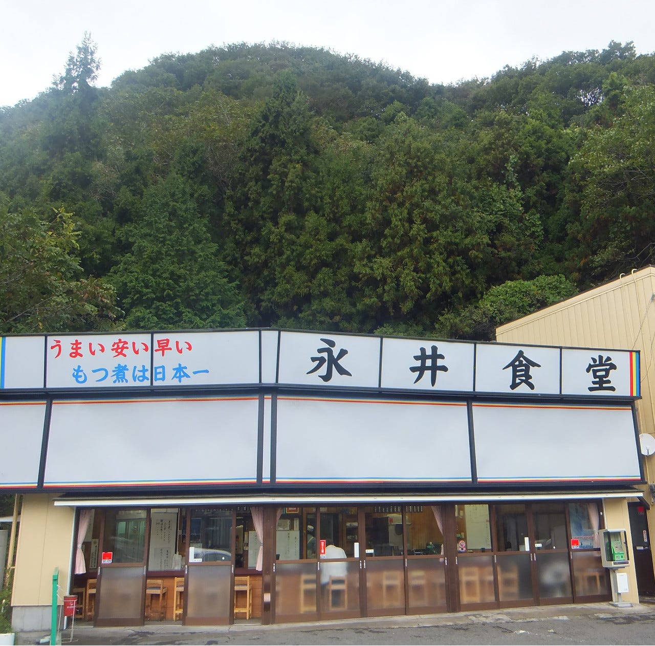 山あいに立つ永井食堂の白いファサード看板と平屋建店舗の全景