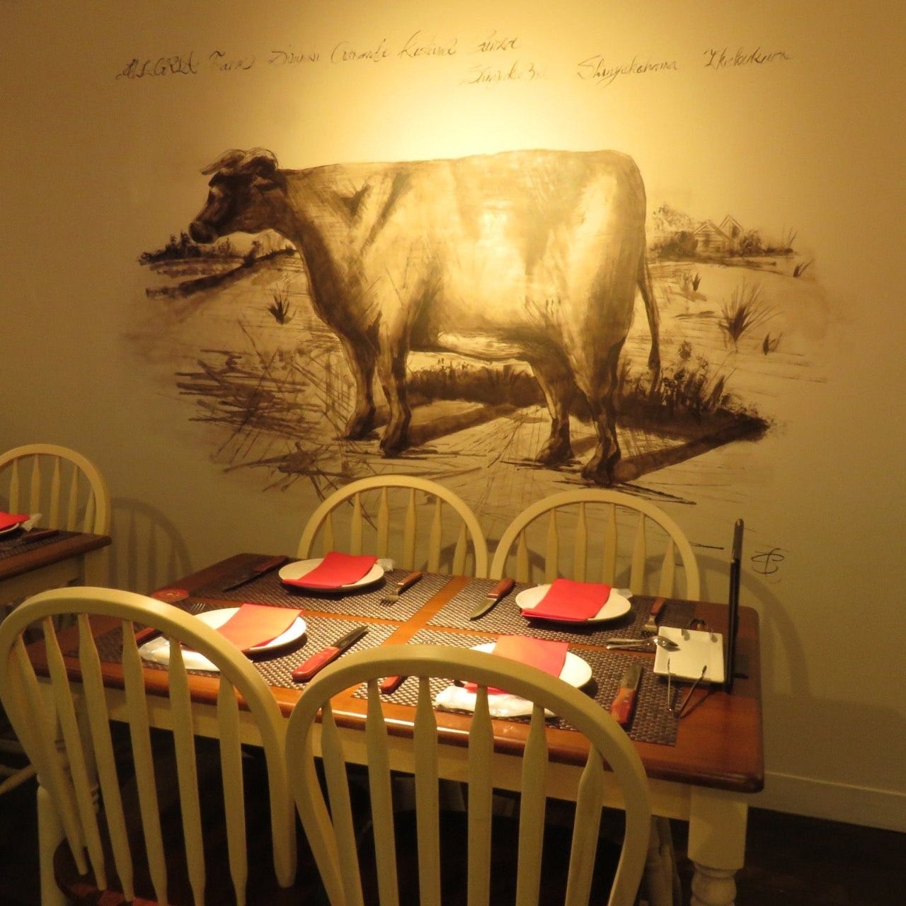 牛が描かれた壁を背景に、皿とナイフ・フォークとナフキンが4人分置かれた4人席