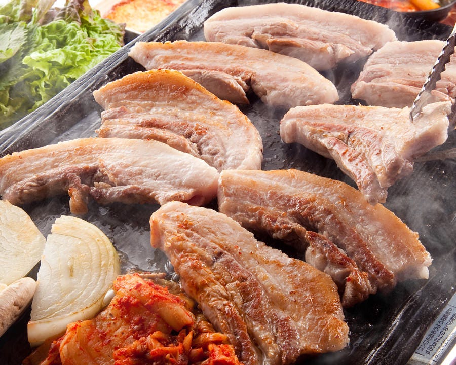 鉄板で焼かれる厚切り豚バラ肉と玉ねぎ、キムチなど