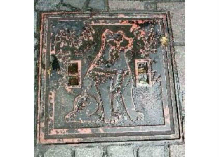 A square cover bearing the image of Hachikō located near the Hachiko statue in Shibuya Station