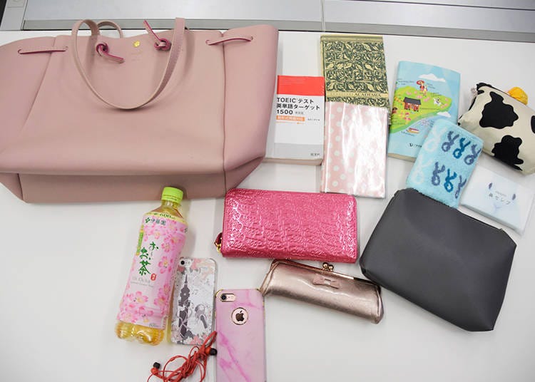 Clockwise from top left: bag, 3 books, a schedule book, a makeup pouch, tissues, a hand towel, a pouch (bag in bag), her wallet, a pen cake, two iPhones, and a bottle.
