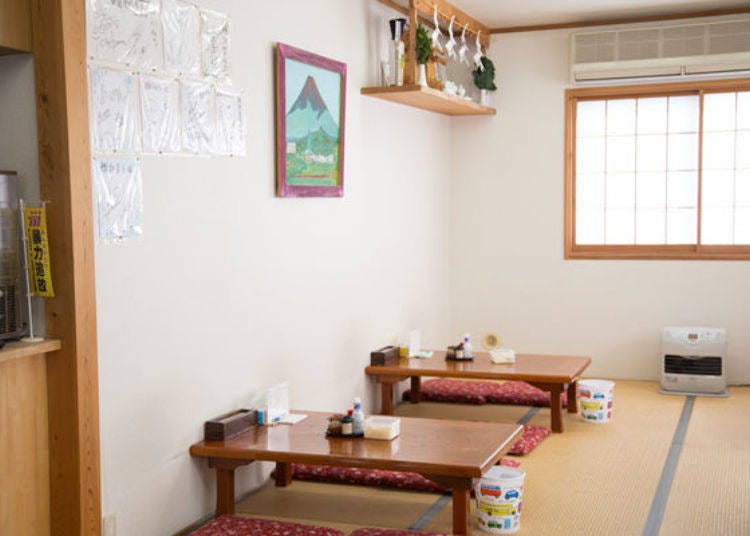 A clean and bright interior with tables stocked with menus, soy sauce, shichimi pepper, crispy tempura flakes, and suridane seasoning.