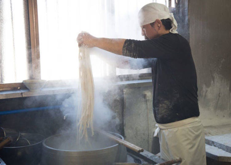 Freshly handmade noodles are swiftly tossed into a large pot for boiling.