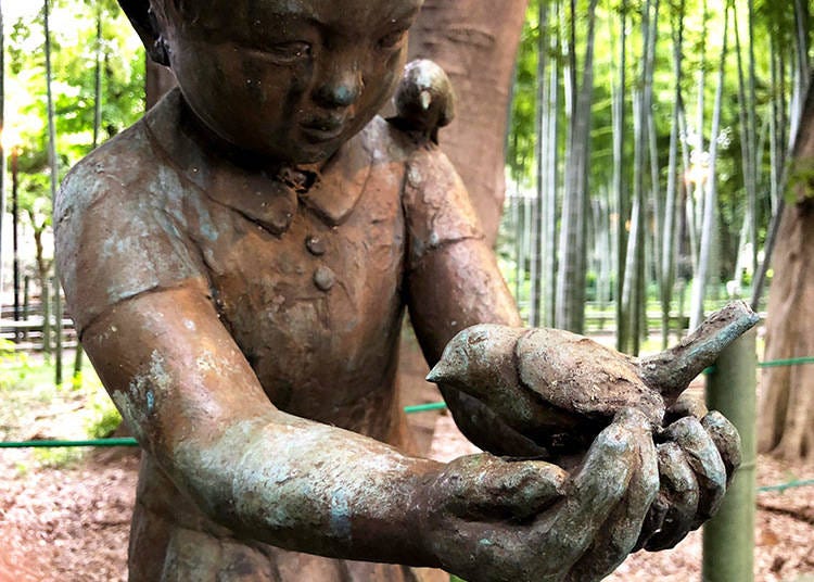 A statue of a child holding a sparrow in this calm bamboo grove