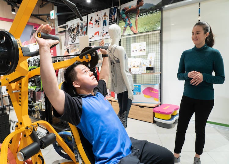 A FITNESS SHOP HARAJUKU staff shows a customer how to use a workout machine.