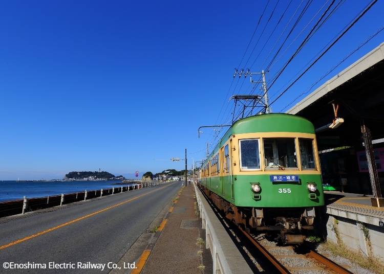 Enoden at Kamakurakokomae Station, with Enoshima Island in the background. ©Enoshima Electric Railway Co., Ltd.