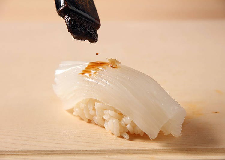 Wasabi is placed on top of finely-cut squid, and soy sauce is applied with a brush.