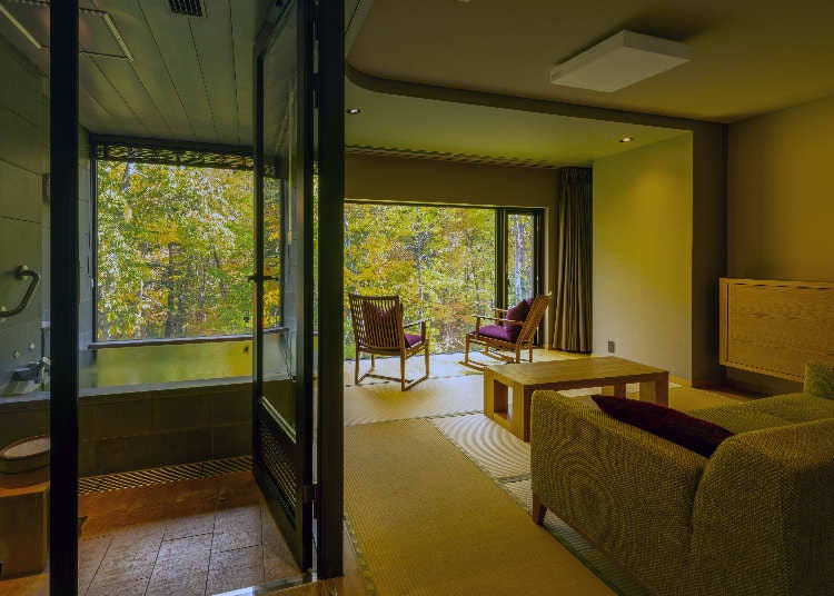 Both the living room and the open-air bath face a wall of large windows. The forest trees that color the room make the window look like a movie theater screen. (Photo provided by: Okujozankei Onsen Kasho Gyoen)