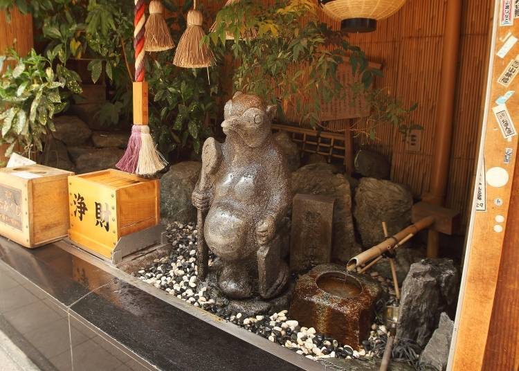 A statue of a tanuki (raccoon dog) in front of a small shrine at 5-chome