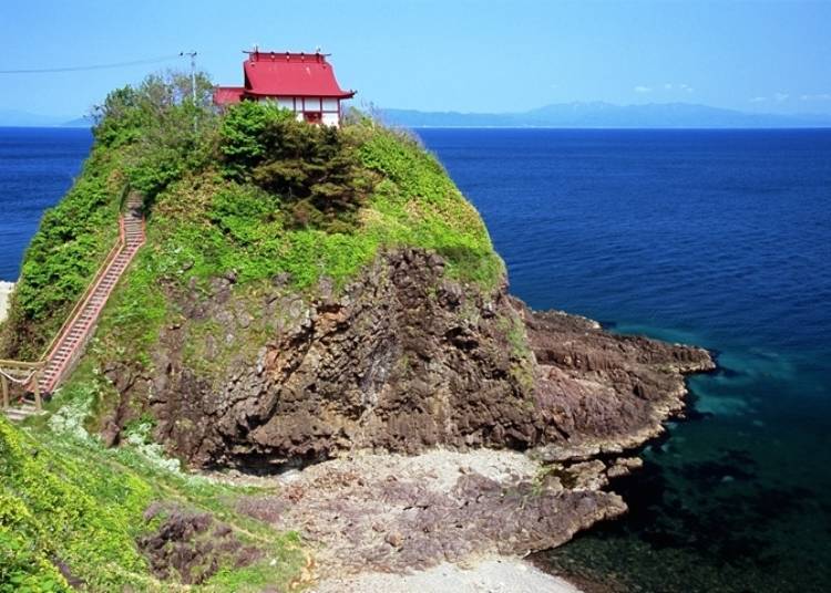 The shrine sits atop a rocky mountain, with the torii at the foot of the steep stairs. The silhouette across the sea is mainland Hokkaido (Photo courtesy of Okushiri Tourism Association)