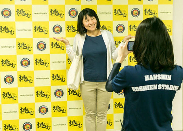 ▲A tour participant posing for a photo in front of the Hanshin Tigers backdrop. It’s OK to wear a Happi coat and bring goods with you.