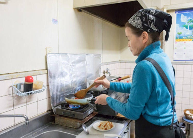 ▲Mrs. Mikiko Morishita, wife of the Takasago Foods president, displays her culinary skills in the kitchen of the dining hall