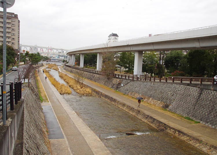 Upstream along the Sumiyoshi River is a water wheel used for polishing rice. Pictured on the right is the Rokko Liner.