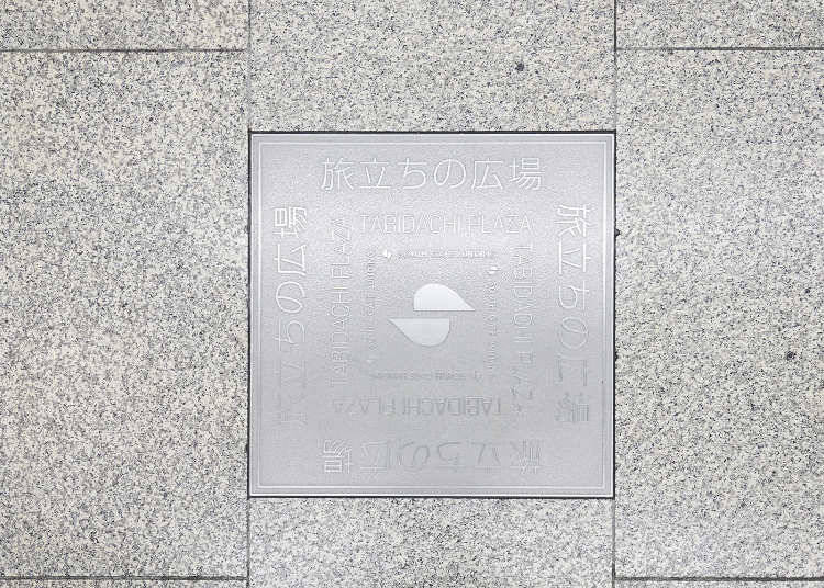 A plaque on the floor with "Tabidachi-no-Hiroba Plaza" engraved on it