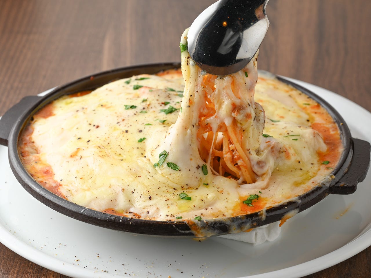 トングで持ち上げているたっぷりチーズの焼きパスタチーズイラプション