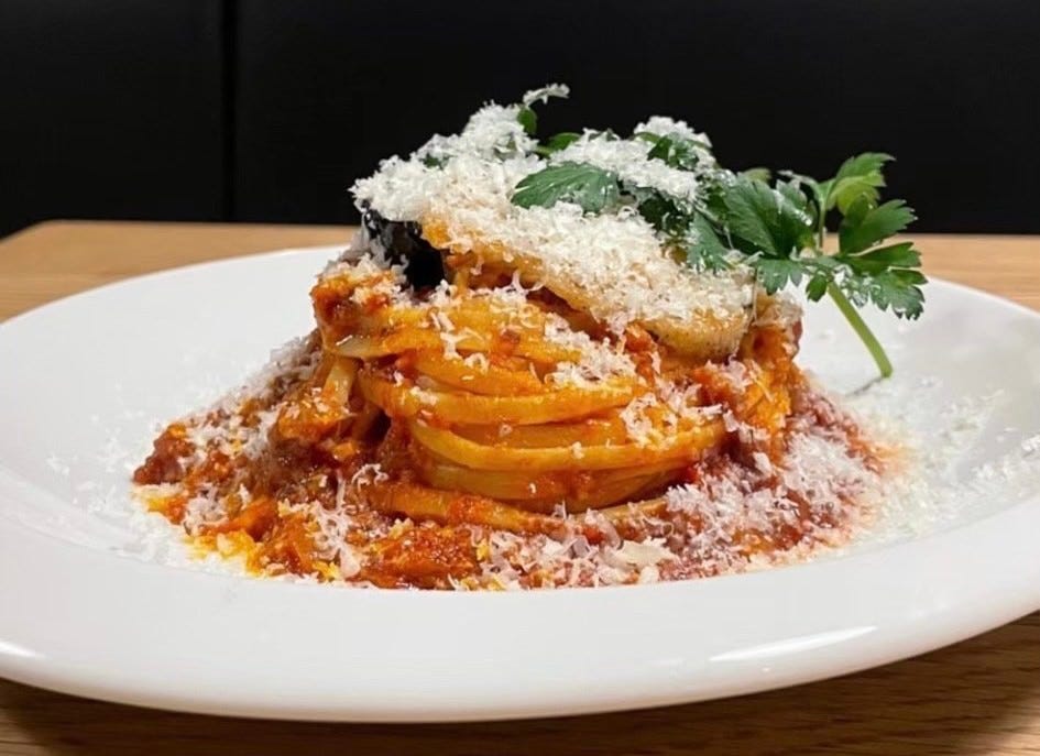 白い皿にのったチーズがたっぷりかかったトマトベースのパスタ