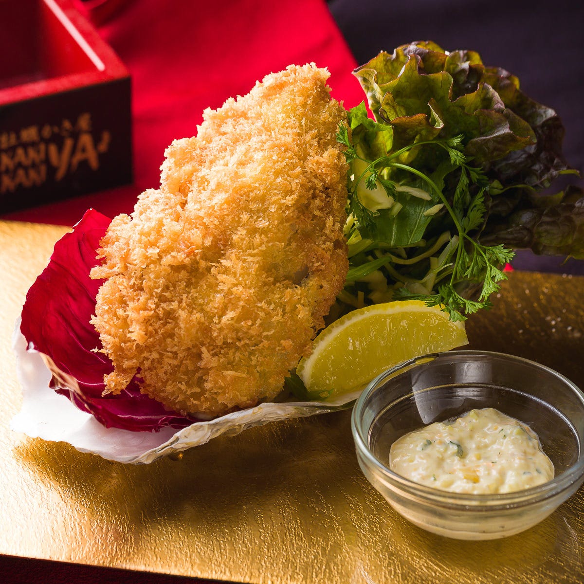 牡蠣フライとタルタルソースが金色のお皿の上に並んでいる