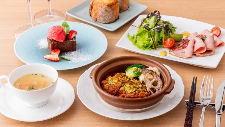 テーブルにメインの肉料理・サラダ・スープ・パン・デザート・白ワインがのっている