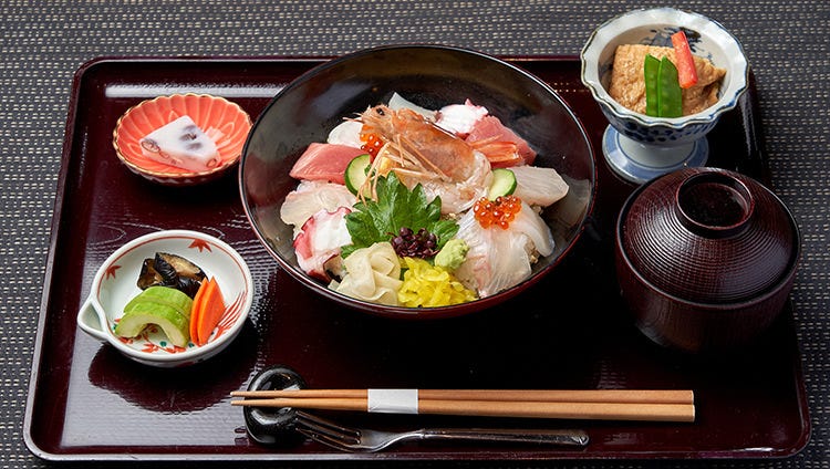 黒いおぼんの上に海鮮丼・漬もの・みそ汁・副菜・デザートがのっている