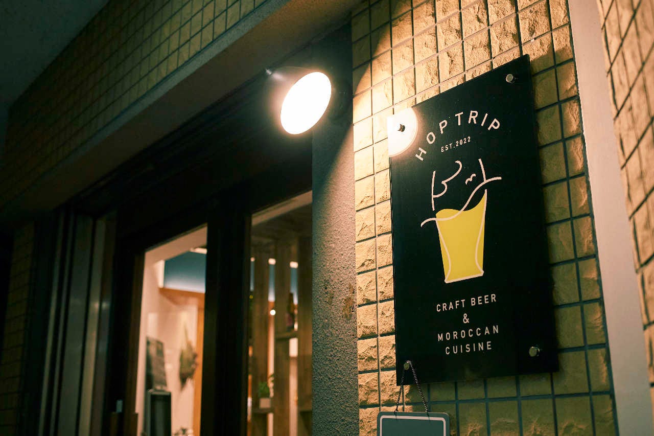店名が書かれた黒い看板がかかった壁面をライトが照らすホップとリップ 与野店の外観