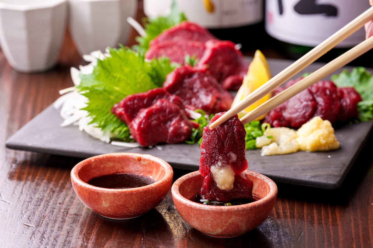 四角い黒のさらに盛られた馬刺しをわりばしで持ち上げる様子