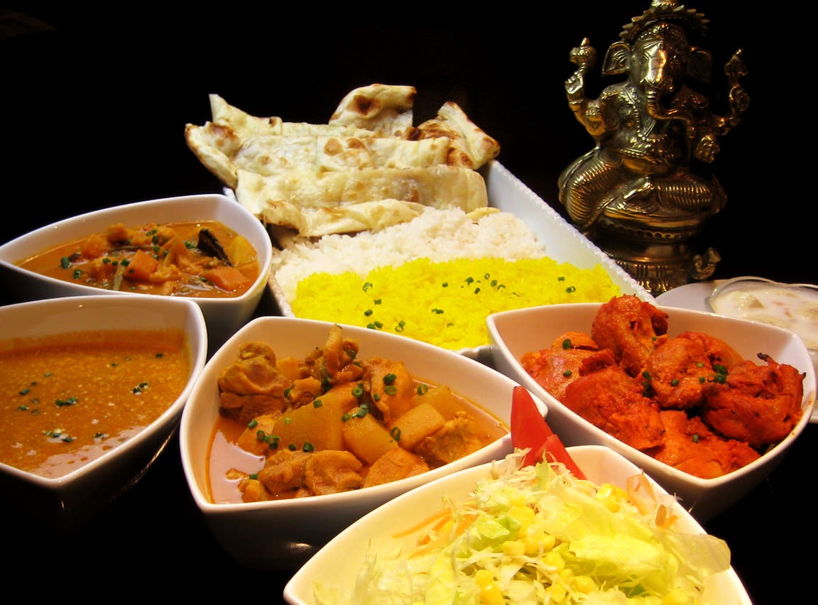 ンド料理のセット。ナン、ライス、カレー、タンドリーチキン、サラダが並び、ガネーシャ像が飾られている。