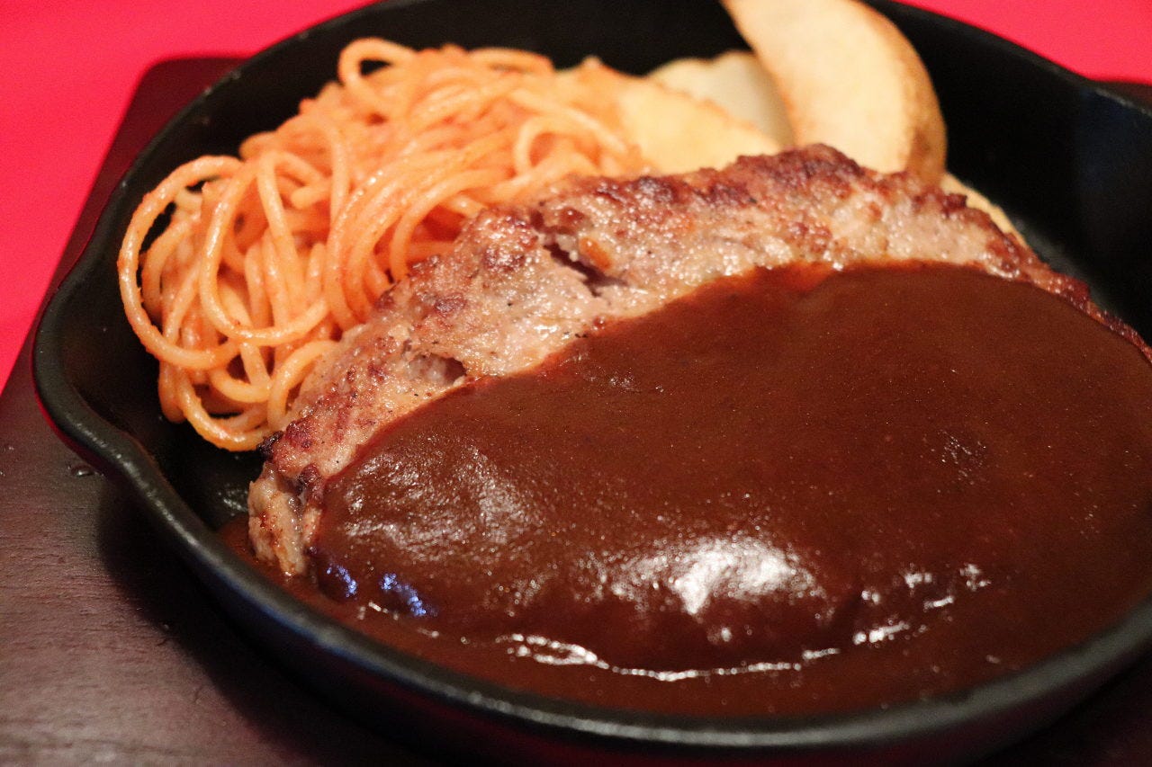 鉄板にデミグラスソースがかかったハンバーグとナポリタン、フライドポテトが盛り付けられている