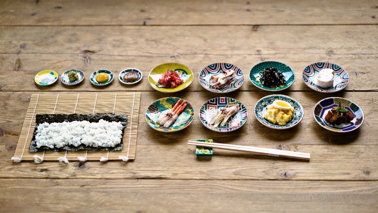 木のテーブルに巻き寿司用のご飯と海苔、具が並んでいる