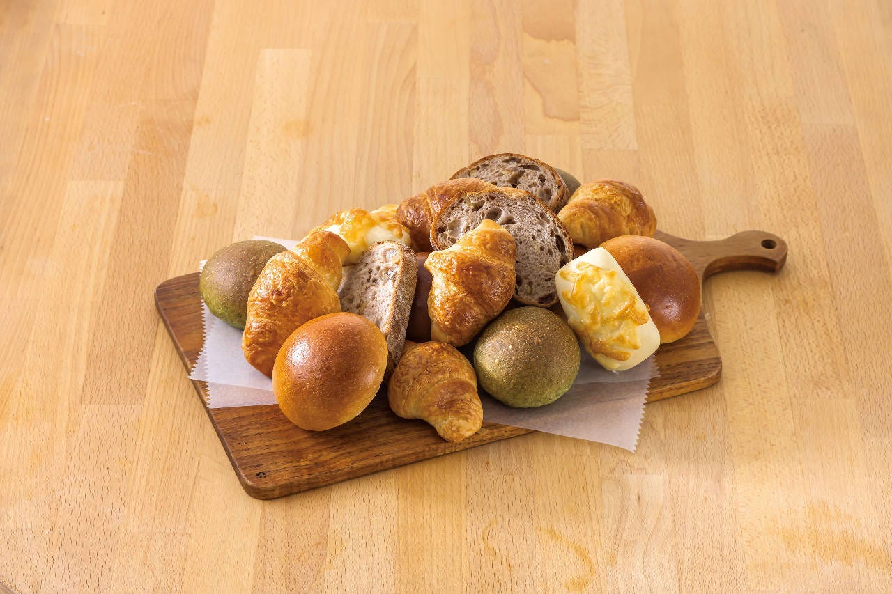 さまざまな種類のパンが木のカッティングボードに盛り付けられている。クロワッサンや丸パン、チーズ入りのパンが並ぶ。