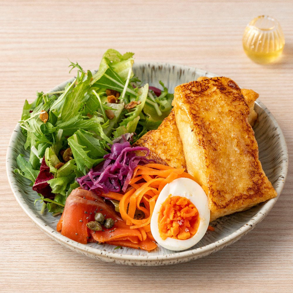 グレーの皿にのったフレンチトースト、ゆで卵、スモークサーモン、キャロットらぺ、リーフ野菜