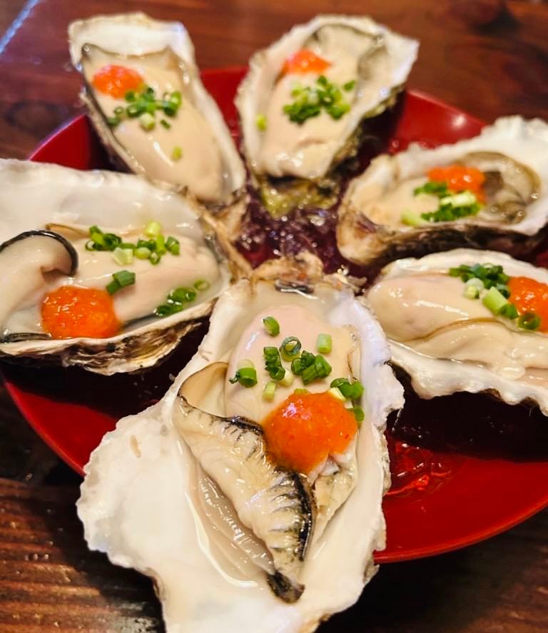 もみじおろしとねぎが添えられた生牡蠣が5個、赤いお皿の上に円形上に並んでいる