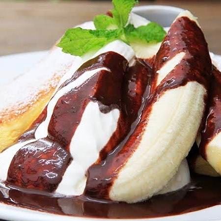 白い皿の上にのったバナナホイップパンケーキチョコソース添え