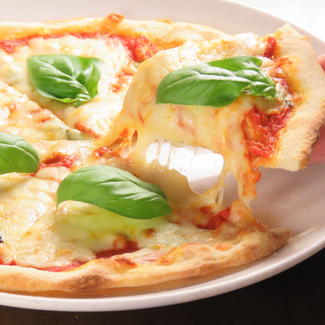 イタリアンバル バンビーノセンター南店のマルゲリータピザを持ち上げている様子