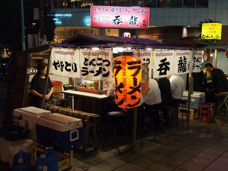 夜、明かりが灯った「屋台 呑龍」。赤い提灯と看板、店名が書かれた白い暖簾が目印