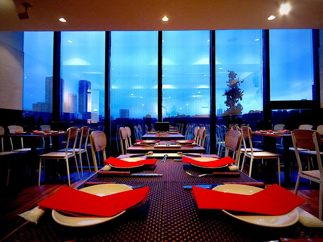 都会の景色を望む壁一面の大きな窓と、赤いナフキンのあるテーブル