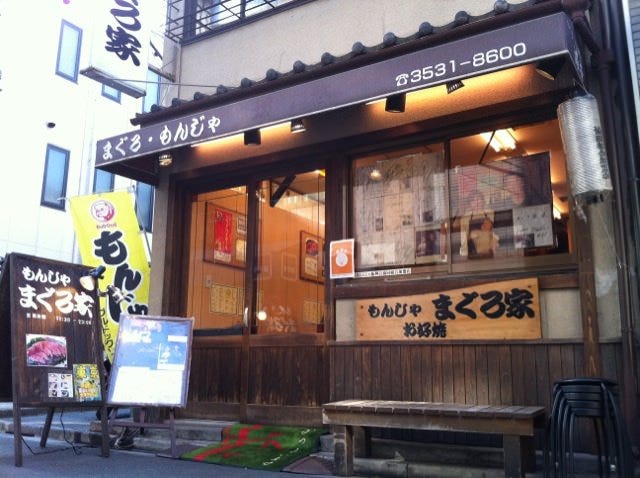 ブラウンの暖簾、まぐろ家と書かれた大きな木の板が特徴的な外観