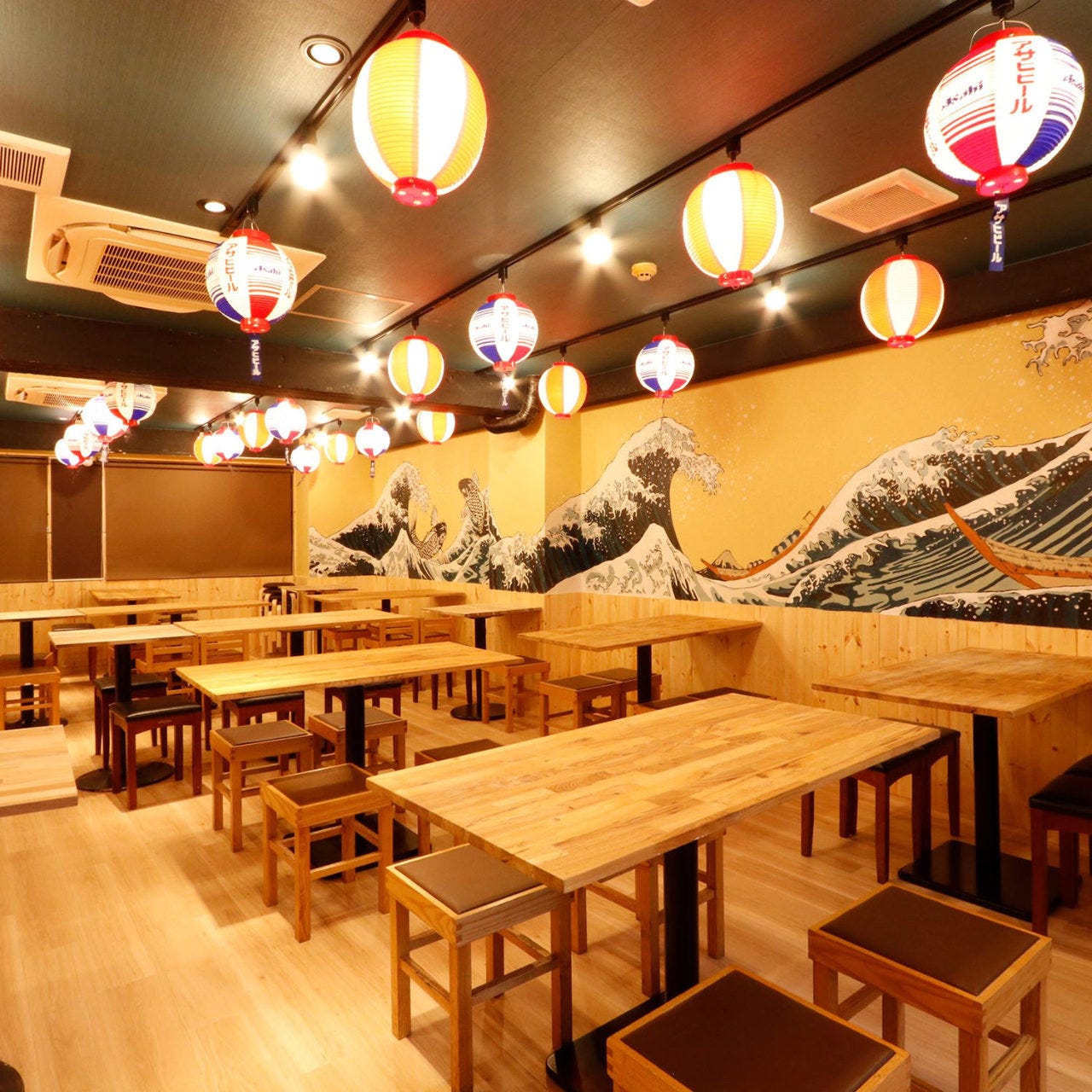 カラフルなちょうちんと和風の空間に、木のテーブルが並ぶ鳥将軍 新橋店店内