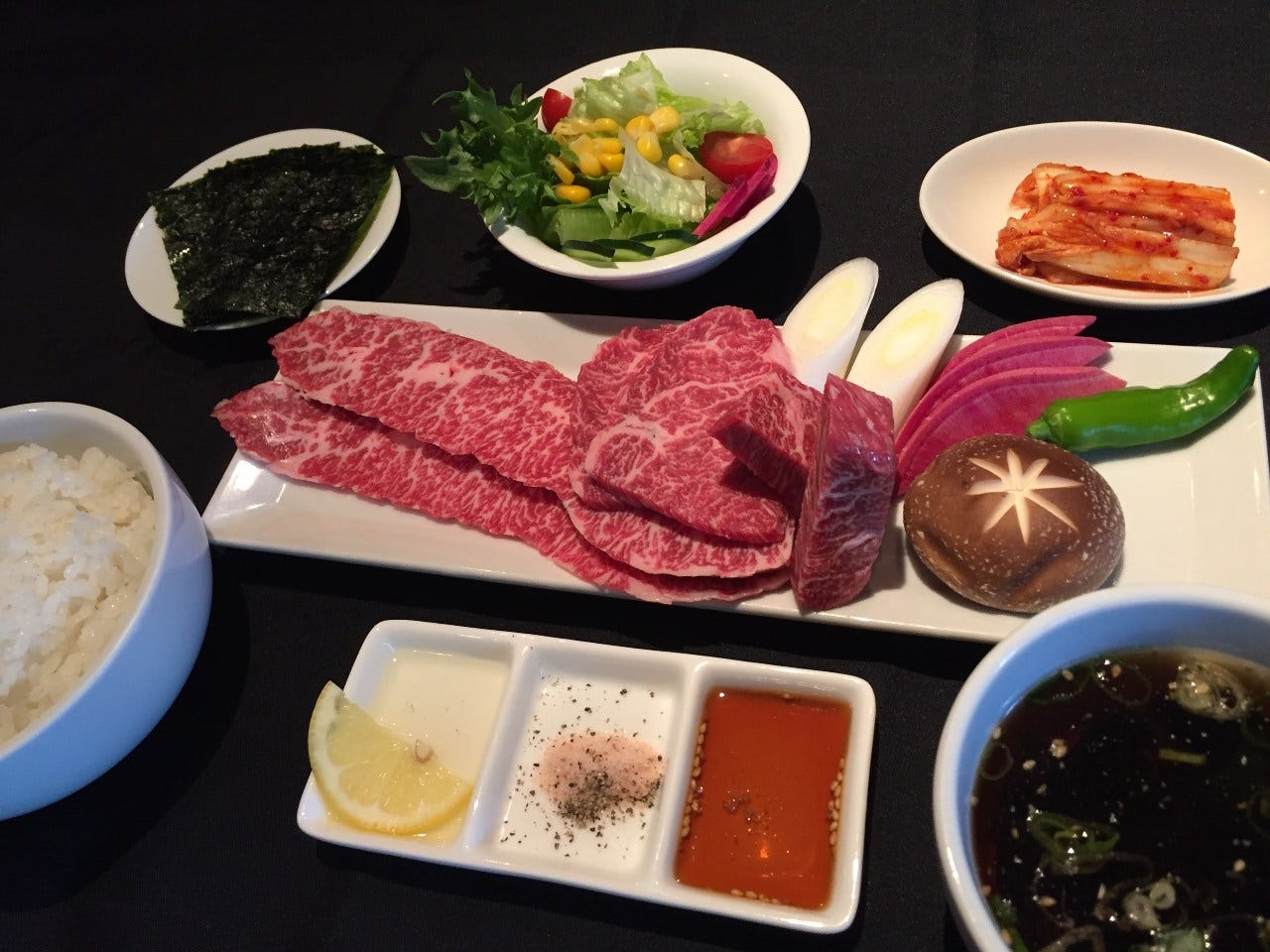 黒いテーブルに焼き肉セットやサラダ、ごはん、スープ、キムチが置かれている
