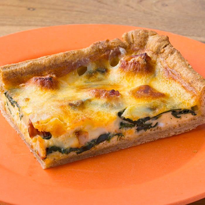 オレンジの皿にのったほうれん草とベーコンのキッシュパイ