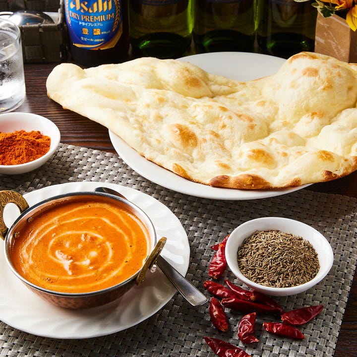 テーブルにナンとバターチキンカレー、香辛料、缶ビール、水が置いてある
