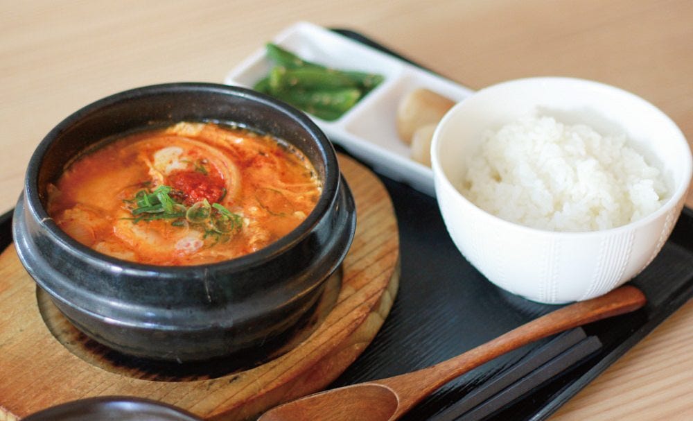 黒いお盆にのったスンドゥブとごはんと付け合わせ