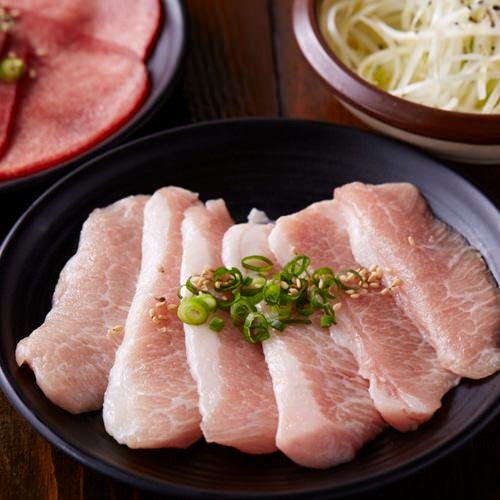 黒い皿に盛り付けられた新鮮な豚肉の薄切り。ネギがトッピングされ、焼肉の準備が整っている。