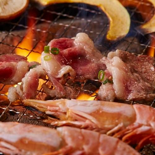 焼き網の上で焼かれている和牛とエビ。炭火で焼かれる香ばしい食材の様子。