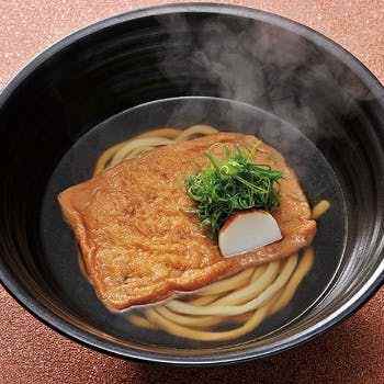 黒いどんぶりにはいった大きな揚げがのったうどん