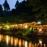 清滝川に架かったつり橋を渡ると清流に張り出して作られた川床があり、京都の市内よりも涼しく過ごしていただける高雄で川床料理をご堪能いただけます。ガラス素材の食器や冷たい食感のお料理、キレイな水で育った鮎など見た目も味も涼しげなお料理をたくさん取り揃えています。お昼は「ミニ会席」もご用意しております！