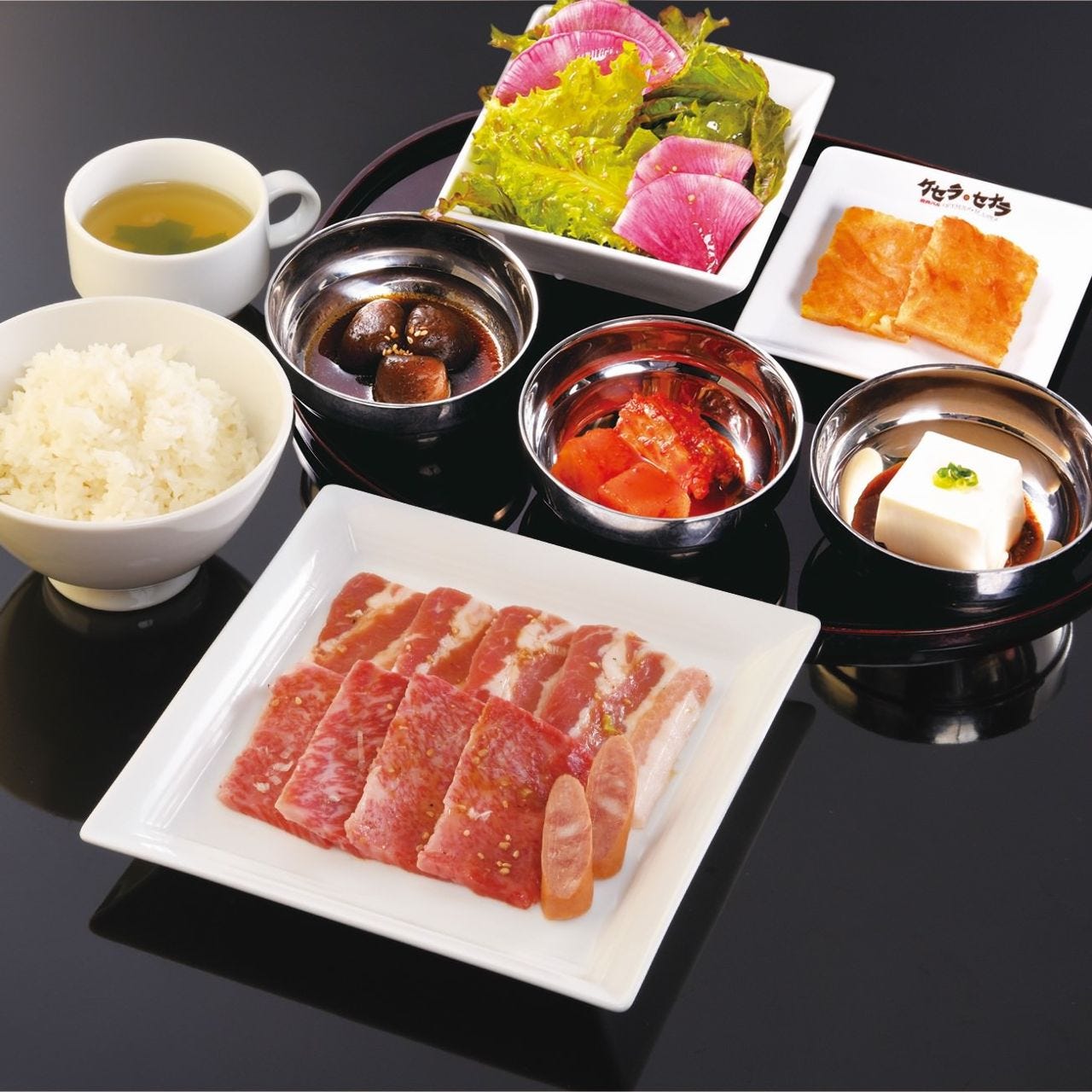 黒いテーブルに焼肉・前菜・サラダ・ごはん・スープが置いてある