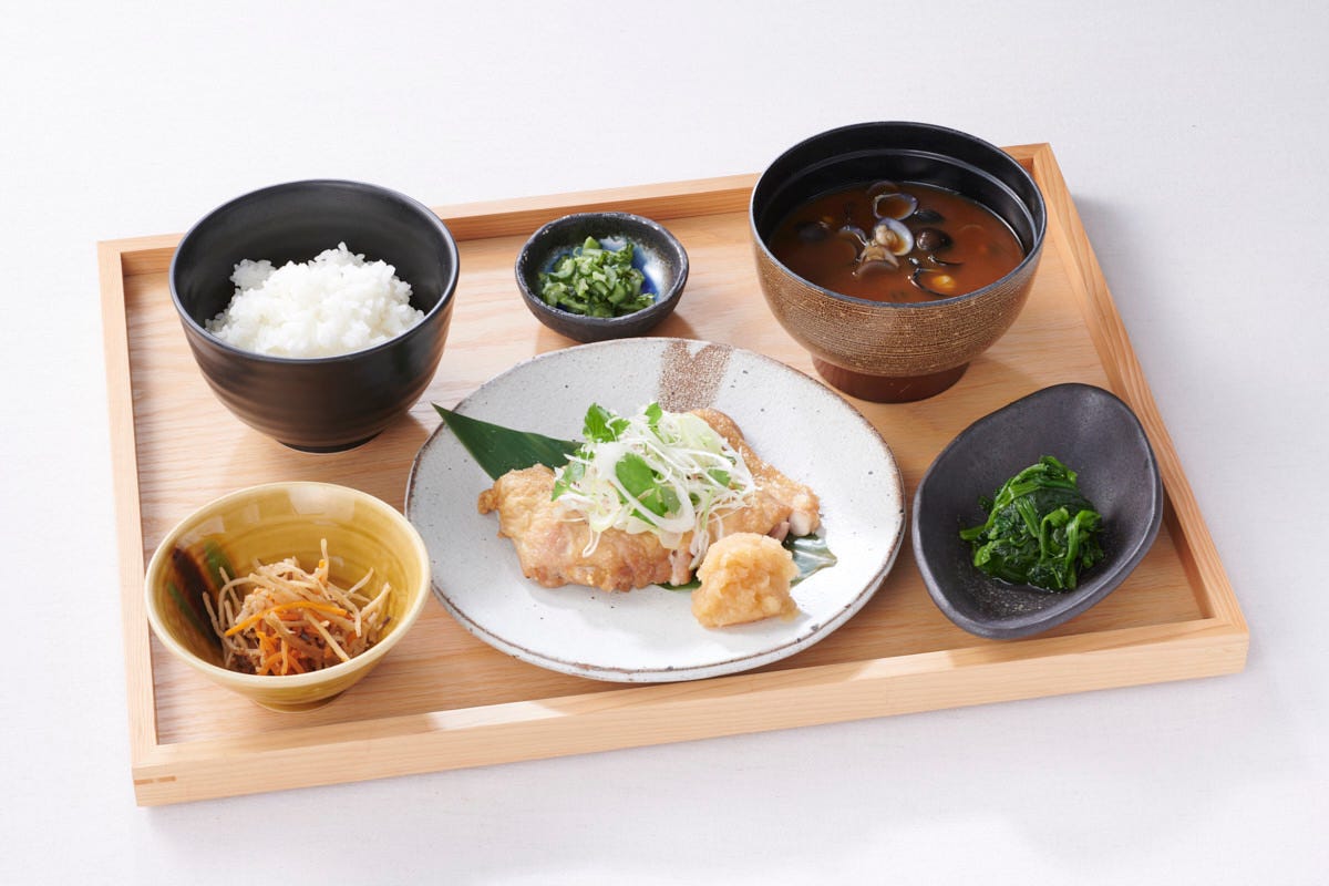 木のお盆にのったお肉料理とご飯と味噌汁と小鉢