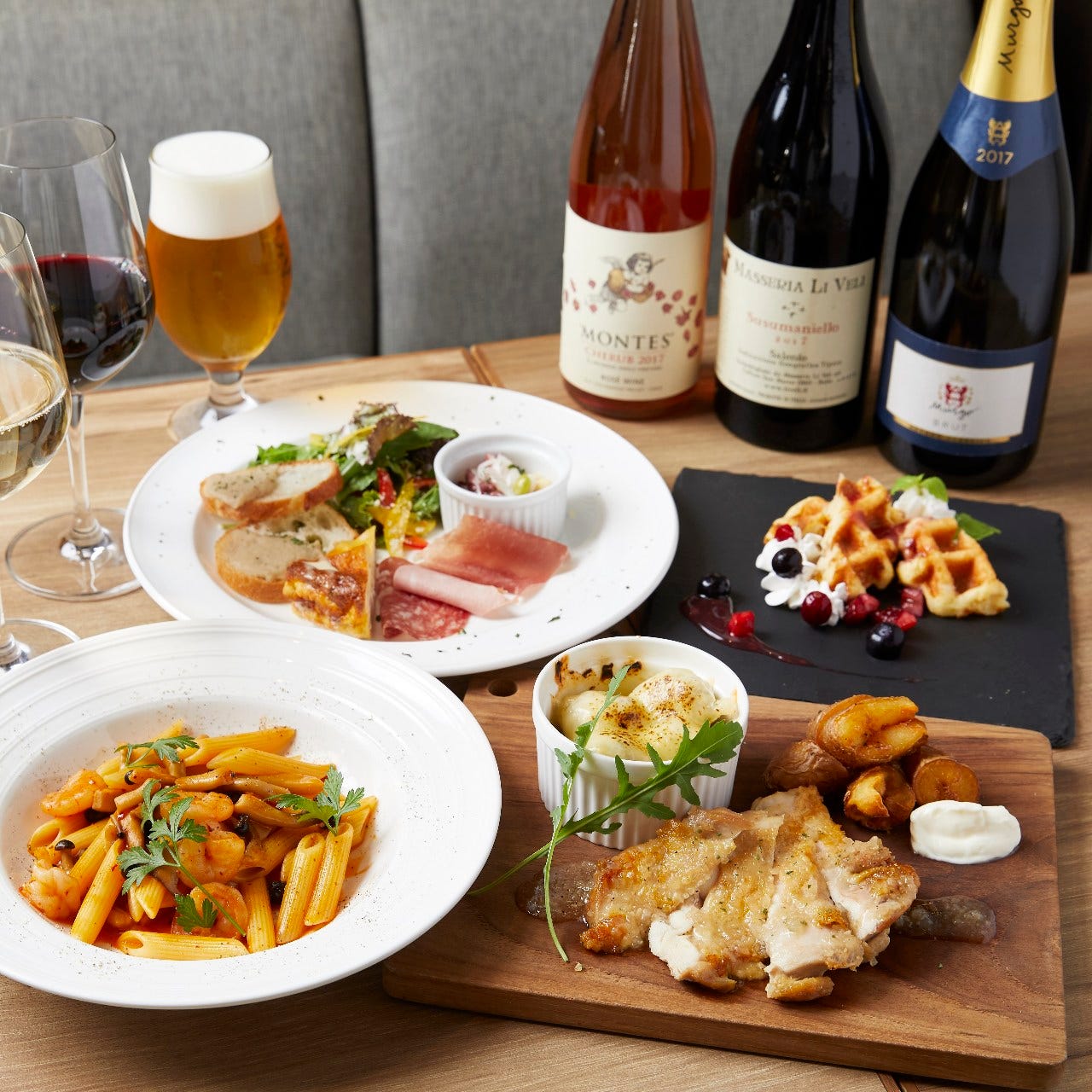 鶏ステーキやパスタ、ワッフルやお酒が並んだテーブル