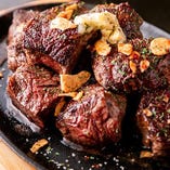 赤身肉の力強い旨みを迫力の分厚さで味わえる「1ポンドステーキ」。1ポンド（約450g）もあるステーキを、プロの火入れ技で赤身の持ち味と柔らかさが際立つレアに焼き上げます。外こんがり＆中ロゼ色の、肉汁溢れるおいしさを、無添加の自家製オニオンソースやニンニク香る塩だれでお楽しみください。