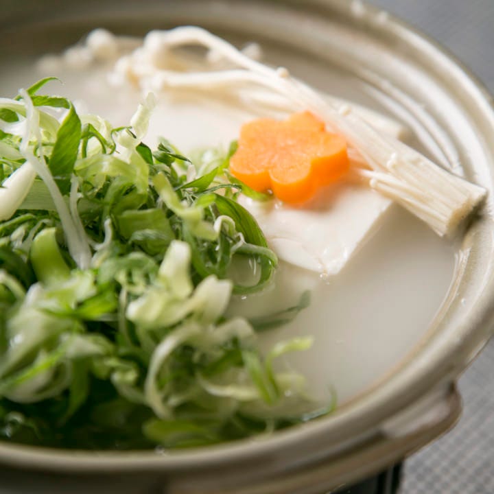 濁ったスープに入った湯豆腐と緑色の野菜